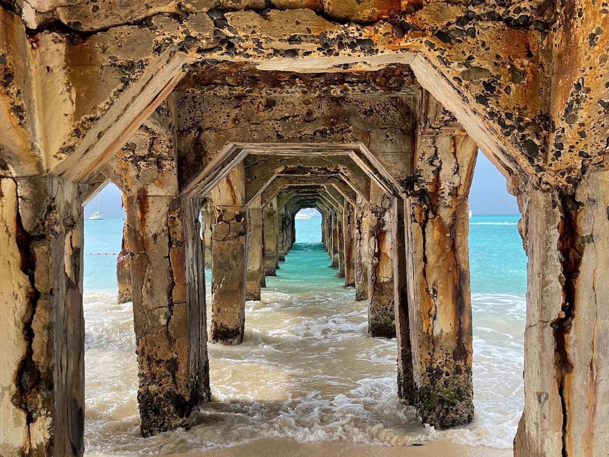View under an ocean pier, showing the blue ocean and sand near The Morgan Resort Spa Village