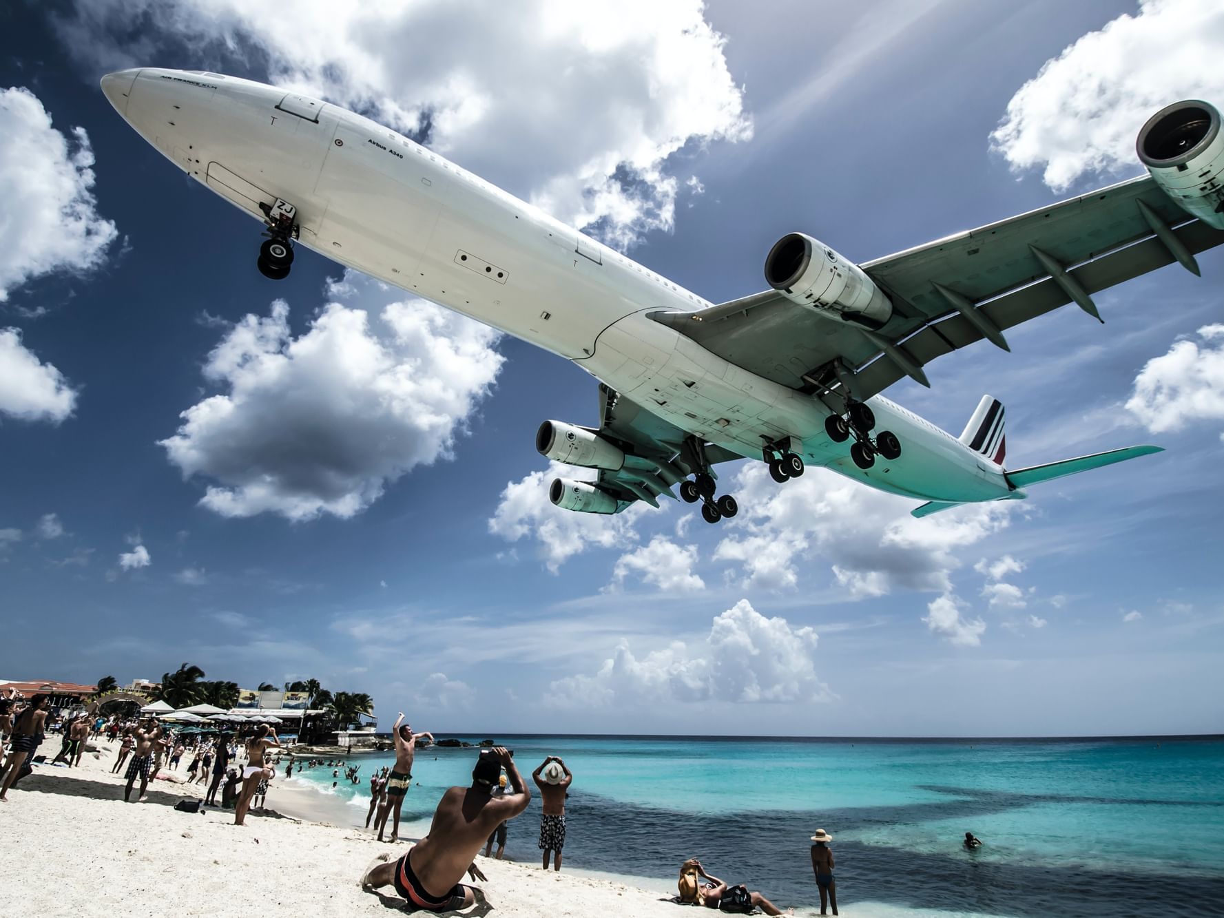 Large white airplane flying low over a Maho Beach with tourists near the water at The Morgan Resort Spa Village